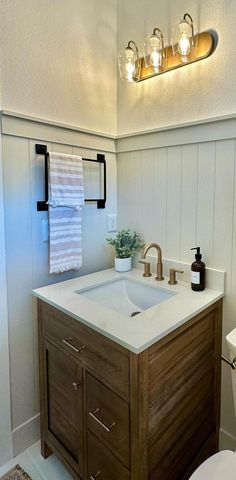 a white toilet sitting next to a bathroom sink under a light over a vanity top