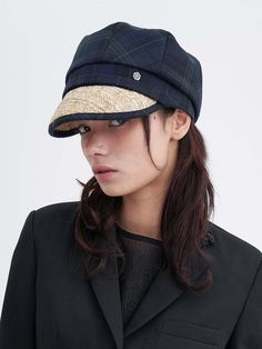 a woman wearing a black jacket and a hat with a plaid pattern on it's brim