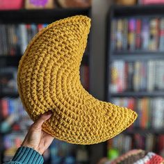 a person holding up a crocheted banana pillow in front of a bookshelf