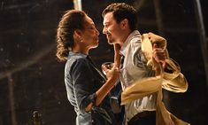 a man and woman standing next to each other in front of a stage holding wine glasses