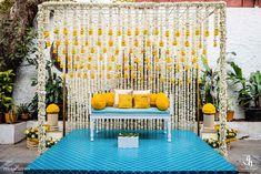 an outdoor ceremony setup with yellow and white flowers on the wall, blue flooring