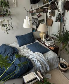 a bed with blue sheets and pillows next to a wall full of books, plants and pictures