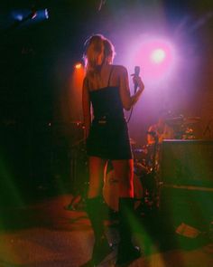 a woman standing on top of a stage next to a microphone and guitar player in front of purple light