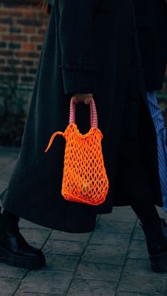 a woman walking down the street with an orange bag on her shoulder and black shoes