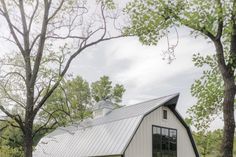 a white barn with a metal roof in the middle of some trees and grass on either side