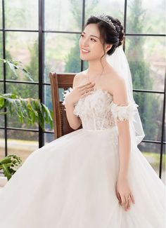 a woman in a white wedding dress sitting on a chair with her hand on her shoulder