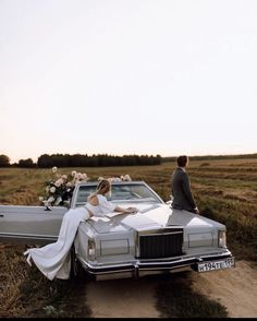 a bride and groom sitting on the hood of a car in a field with flowers