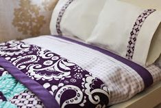 a bed with purple and white sheets on it