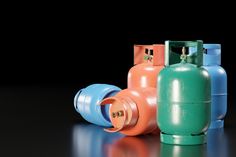 four different colored propane tanks sitting side by side on a reflective surface in front of a black background