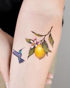 a woman's arm with tattoos on it and a hummingbird flying by an orange