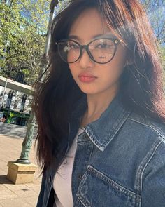 a woman wearing glasses standing next to a street light and tree in the background with her hair blowing back