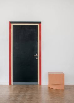 an empty room with a black door and red trim on the wall next to a cardboard box