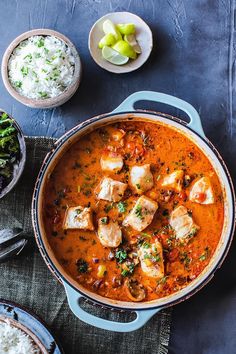 a pan filled with food next to rice and other dishes on a table top,