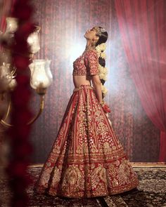 a woman in a red and gold lehenga standing next to a chandelier