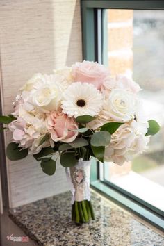 a bouquet of white and pink flowers sitting on a counter next to a window sill