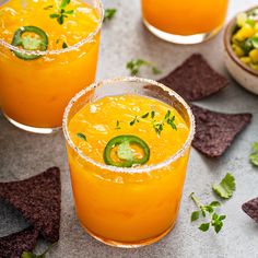 two glasses filled with orange drinks and garnished with jalapenos