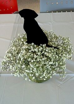 a black dog sitting on top of a vase filled with white baby's breath