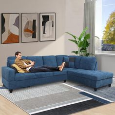 a man laying on top of a blue couch in a living room next to a window