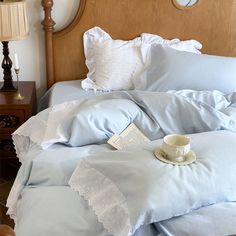 a bed with blue sheets, pillows and a cup of coffee on the end table