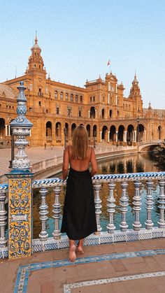 a woman is standing on a bridge looking at the building in the back with blue and yellow tiles