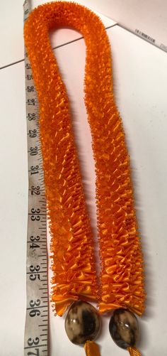 an orange beaded necklace with two beads on it and a measuring tape in the background