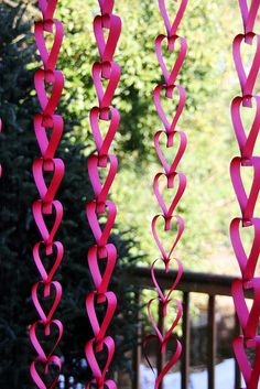 some pink hearts are hanging from the side of a porch railing with trees in the background