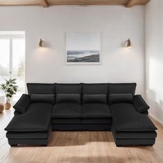 a large black sectional sofa in a living room with wood flooring and white walls