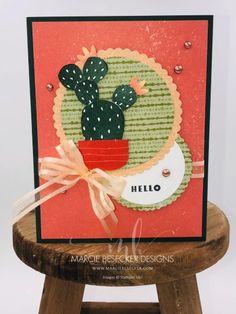 a card with a cactus in a pot on top of a wooden stool and the words hello