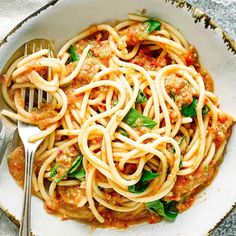 a white bowl filled with pasta and sauce on top of a table next to a fork