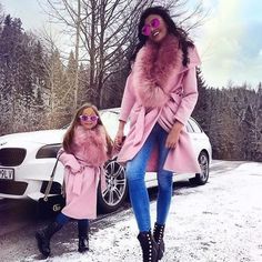 a mother and daughter walking in the snow with their pink coats on, holding hands