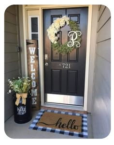 a black door with a welcome mat and white flowers on the front porch next to it