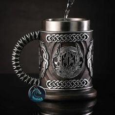 a stainless steel beer mug with an intricate design on the front and sides, filled with water