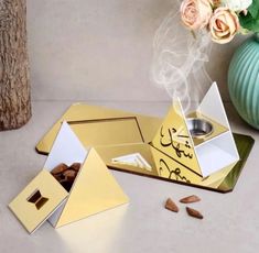 a gold and white box sitting on top of a table next to a vase filled with flowers