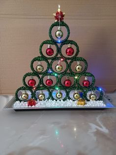 a christmas tree made out of ornaments on top of a white table with a red and green ornament