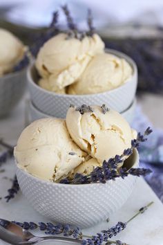 three bowls filled with ice cream and lavender sprinkled on the table next to two spoons