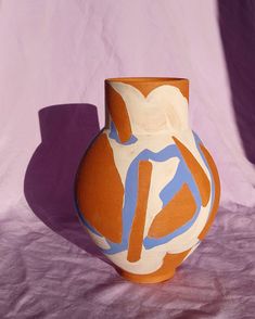 an orange and blue vase sitting on top of a purple cloth covered table next to a white wall