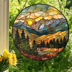 a stained glass sun catcher hanging from a window with mountains and trees in the background