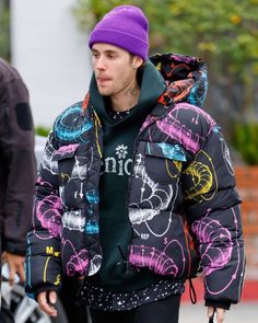 a man in a purple beanie is walking by a car