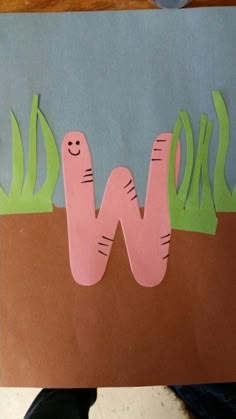 paper cut out of the shape of a worm and grass on top of a piece of cardboard