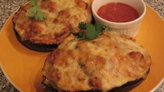 two stuffed eggplant sandwiches on a yellow plate with a small bowl of dipping sauce