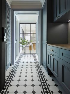 a long hallway with black and white flooring next to blue cupboards, potted plant on the far wall