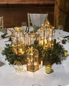 a table topped with lots of glass vases filled with flowers and greenery covered in lights