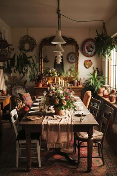 a dining room table with flowers and candles on top of it, surrounded by potted plants