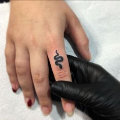 a person with a small tattoo on their ring finger and the word snake written in black ink