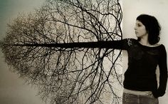 a woman standing in front of a tree with no leaves on it's branches