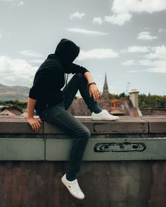 a man sitting on top of a roof with his head down and wearing a hoodie