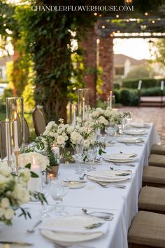 a long table is set with white flowers and candles for an elegant wedding reception in the garden