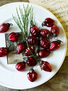 a white plate topped with lots of red glass ornaments and greenery next to sheet music