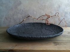 a black bowl sitting on top of a wooden table next to a plant in it