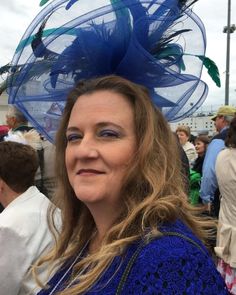 a woman wearing a large blue hat with feathers on it's head at an outdoor event